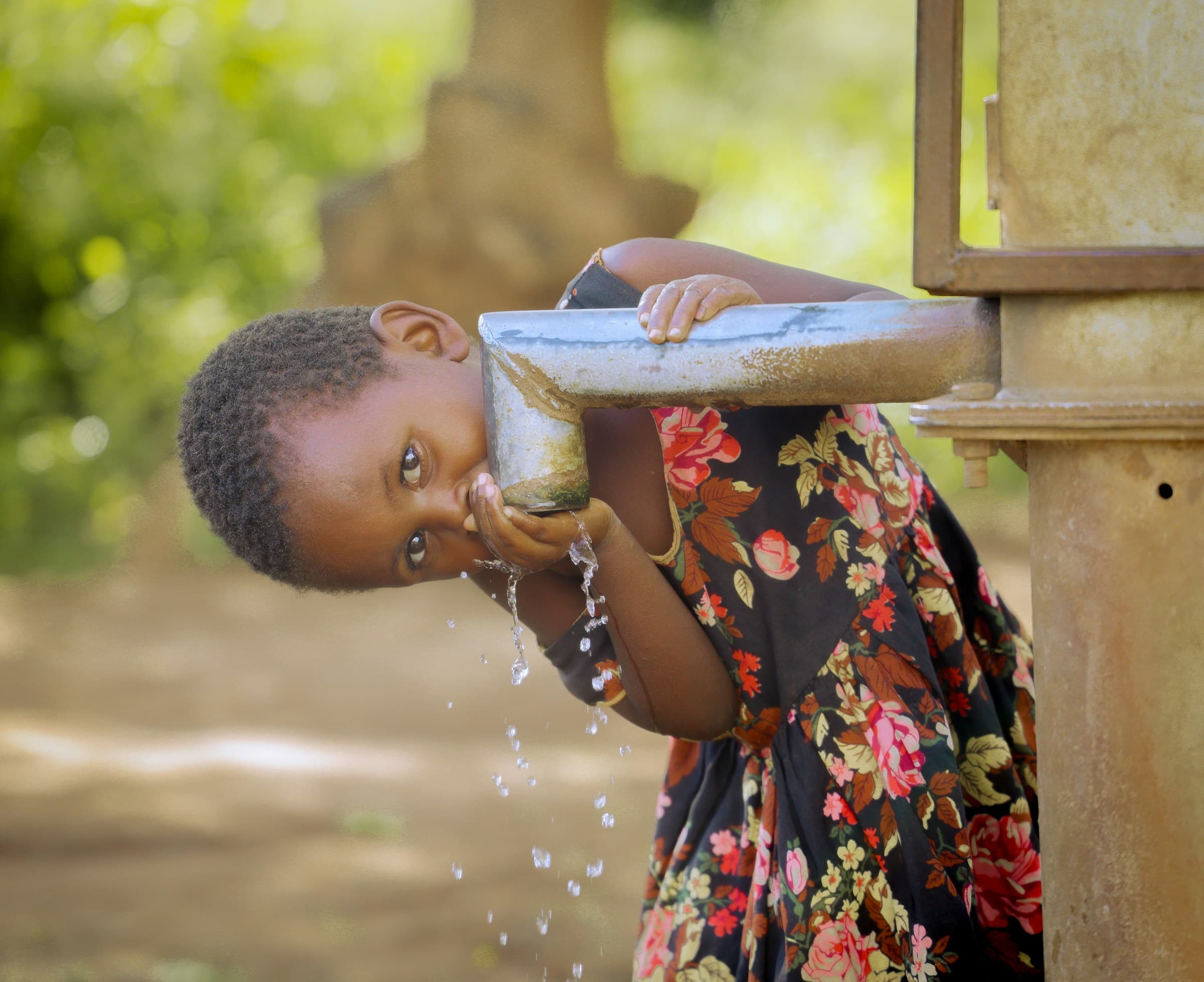 An African child smiling while drinking clean water from a village hand pump