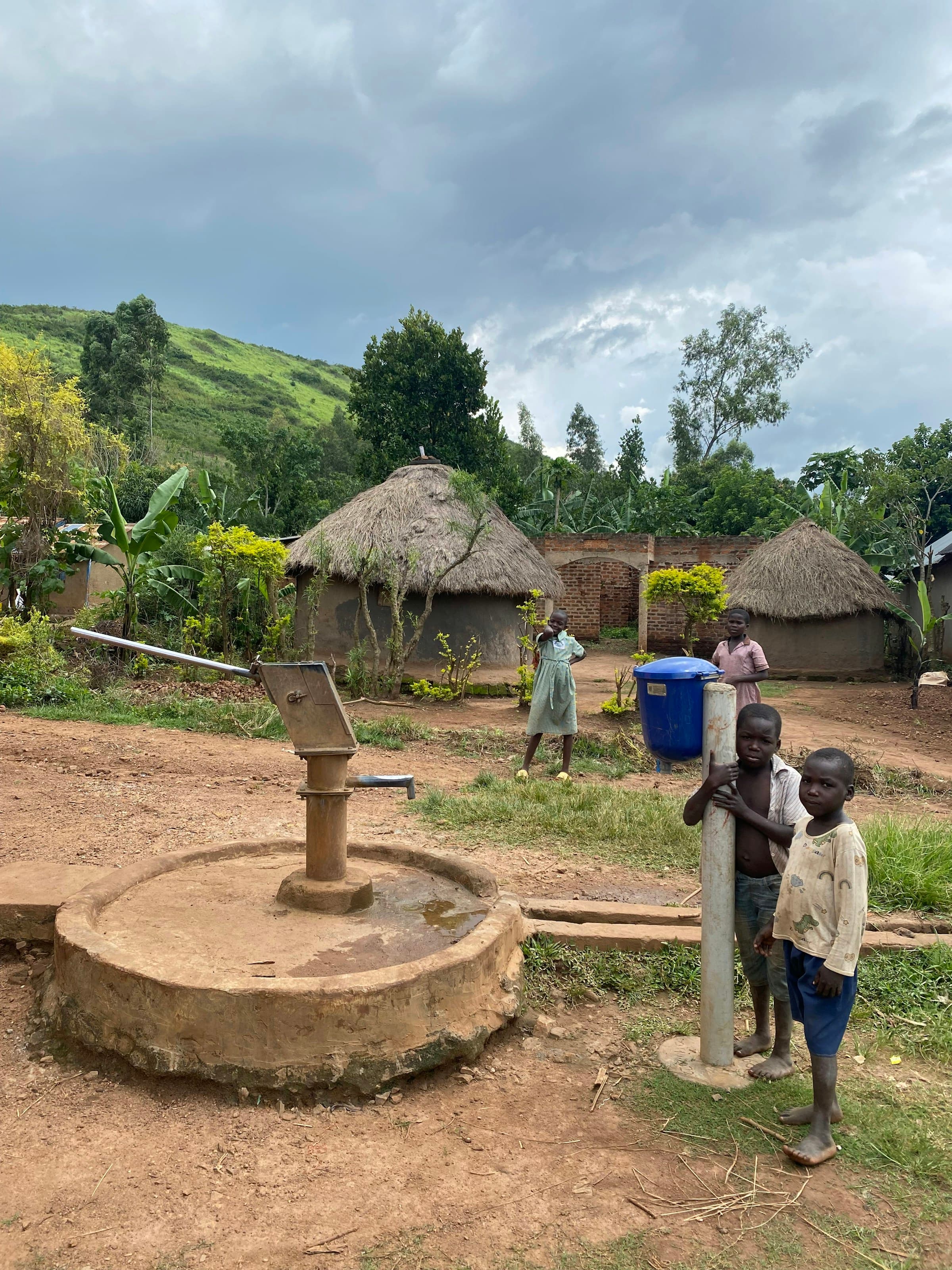 African children standing beside their village water well and hand pump